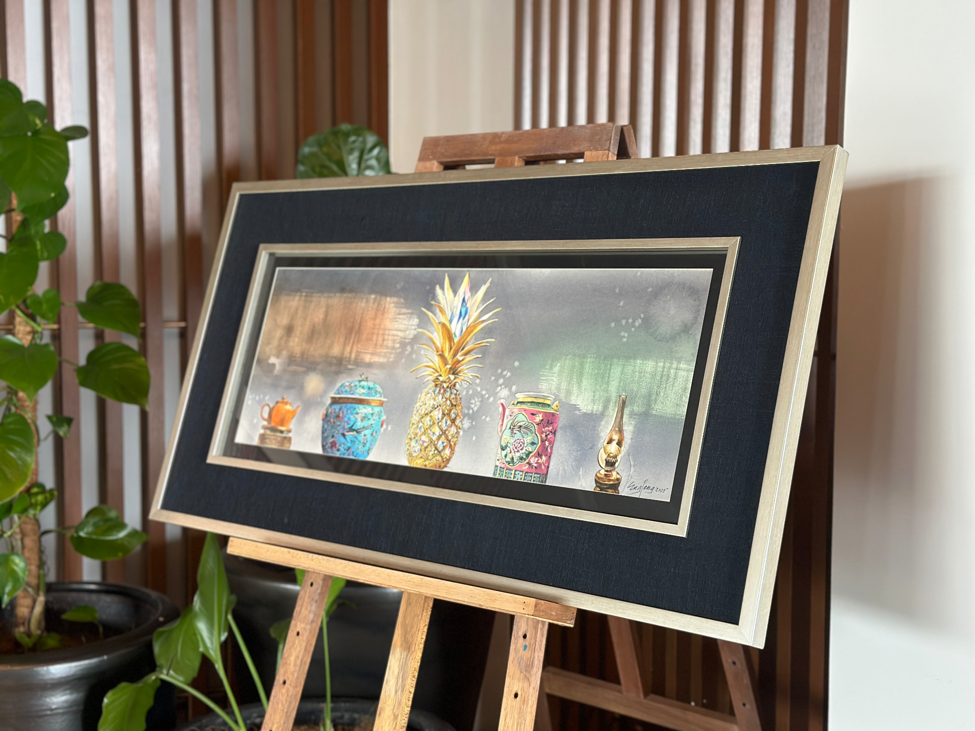 Framed still-life artwork displayed on a wooden easel at Alila Bangsar