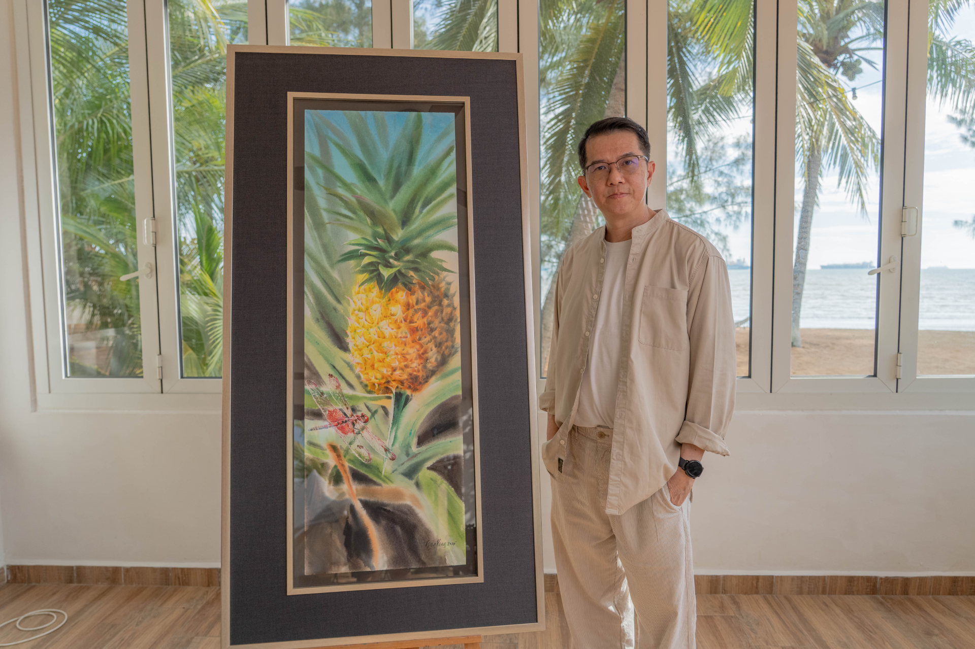 Yeo Eng Peng standing beside his framed watercolour pineapple painting